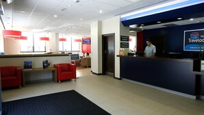 A reception area with a blue counter, red chairs, and a TV screen. - Travelodge Valencia Aeropuerto (Manises)