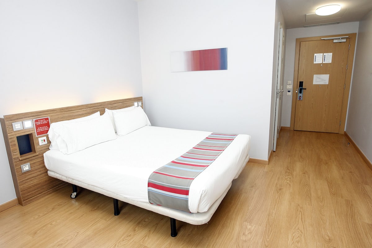 A neatly made bed with a striped blanket, a wooden headboard, and a bedside table with a red sign.