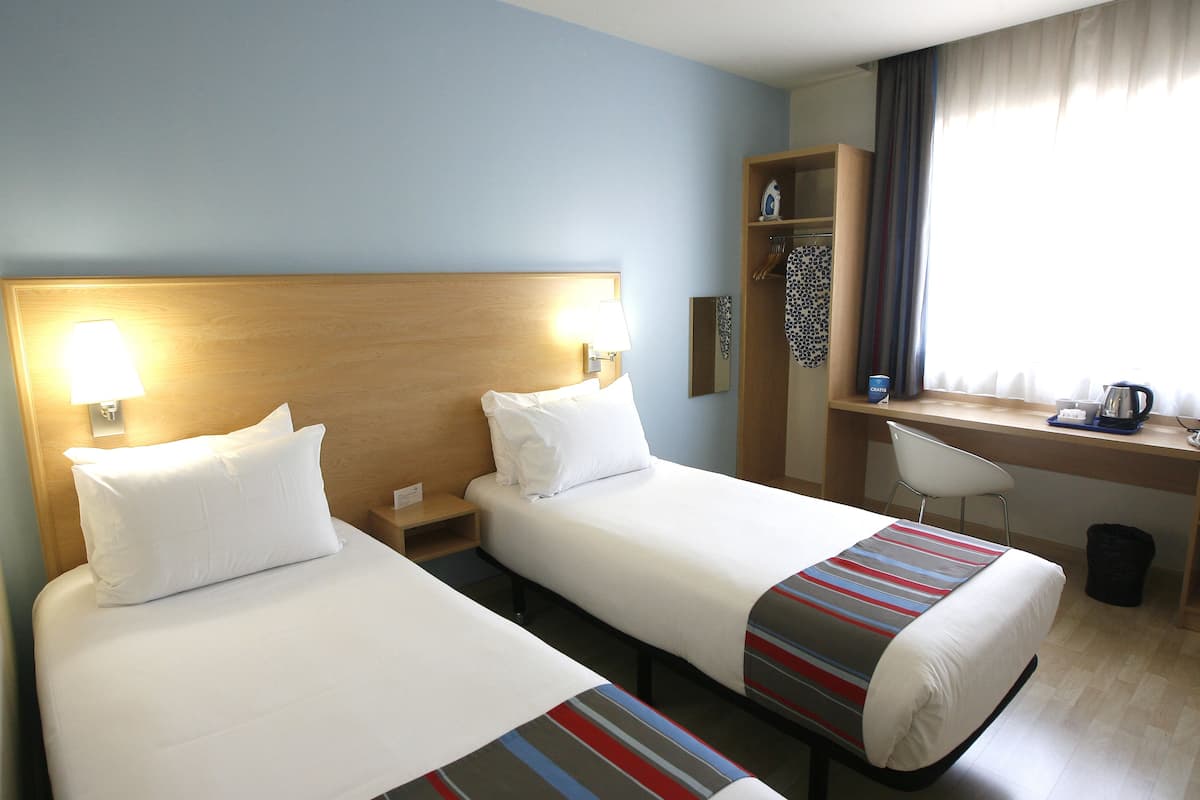 A hotel room with two beds, a desk, a chair, and a window with curtains.