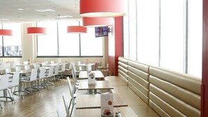 A modern dining area with high tables, benches, and red pendant lights. - Travelodge Valencia Aeropuerto (Manises)