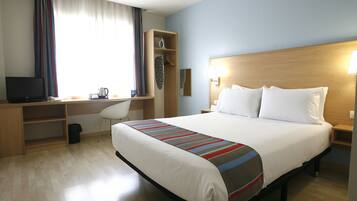 Una habitación de hotel con cama, escritorio con silla, televisión y lámpara.