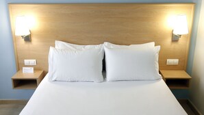 A neatly made bed with white linens and two pillows, flanked by wooden nightstands with wall-mounted lamps. - Travelodge Valencia Aeropuerto (Manises)