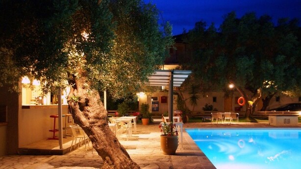A poolside area with a tree, outdoor seating, and a building with a bar. - Thalero Holidays Center (Lefkada)