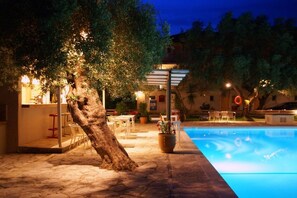 A poolside area with a tree, outdoor seating, and a building with a bar. - Thalero Holidays Center (Lefkada)