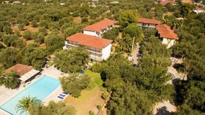 An aerial view of a residential area with a swimming pool, surrounded by trees and houses with red-tiled roofs. - Thalero Holidays Center (Lefkada)