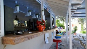 A bar area with a wooden counter, hanging plants, and colorful stools. - Thalero Holidays Center (Lefkada)