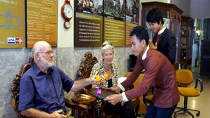 A group of people in a room with a marble wall, a clock, and informational posters. - Royal Hotel (Battambang)