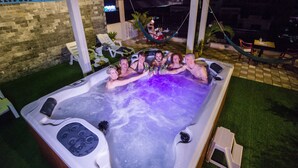 A hot tub with people around it, a hammock, and a poolside area with chairs and tables. - Royal Hotel (Battambang)