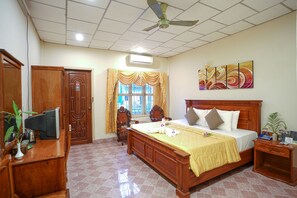 Una habitación de hotel con una cama grande, muebles de madera, un televisor y un ventilador de techo.