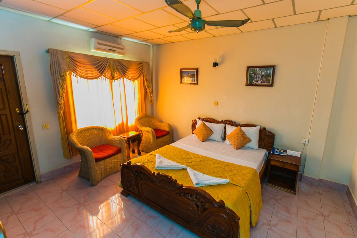A hotel room with a large bed, a chair, a nightstand, and a ceiling fan.