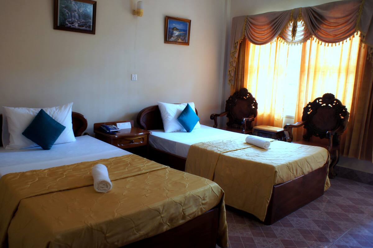 A hotel room with two single beds, a wooden nightstand, a chair, and a desk with a telephone.