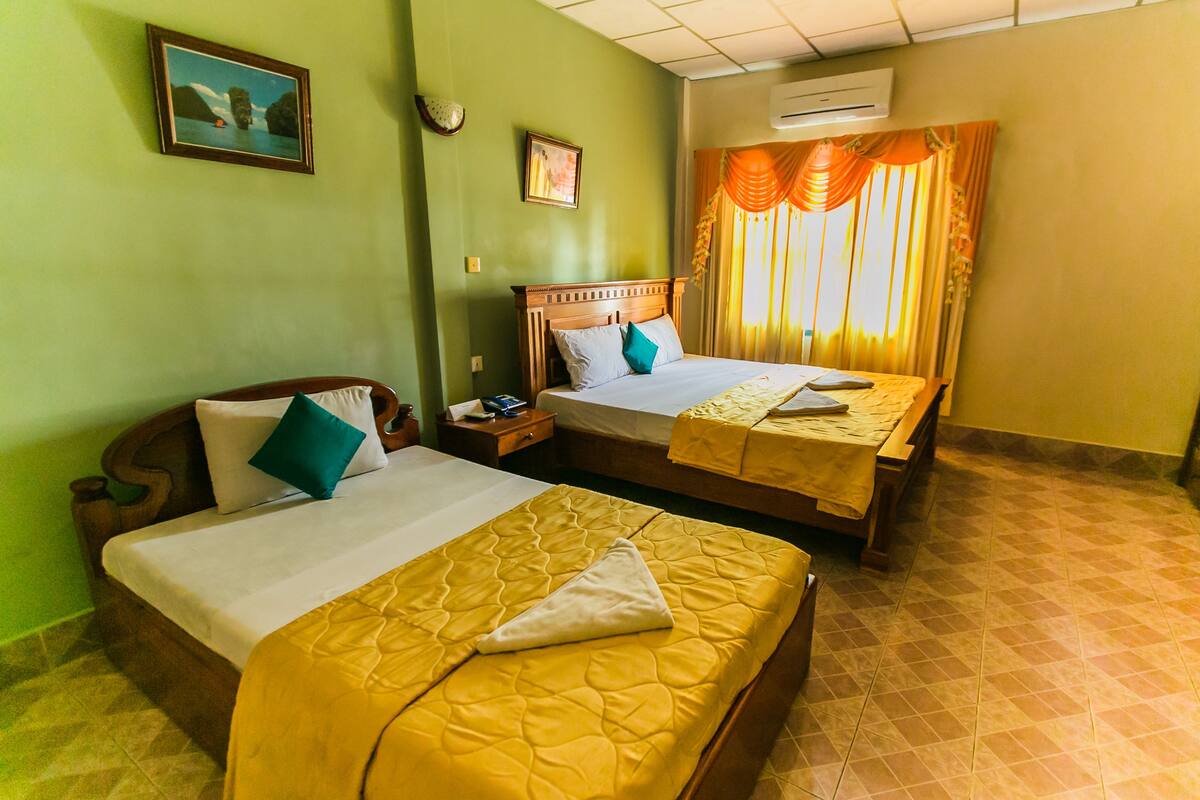 A hotel room with two beds, a nightstand, a wall clock, and a window with curtains.
