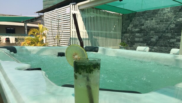 A hot tub with a drink in the foreground, surrounded by lounge chairs and a stone wall. - Royal Hotel (Battambang)