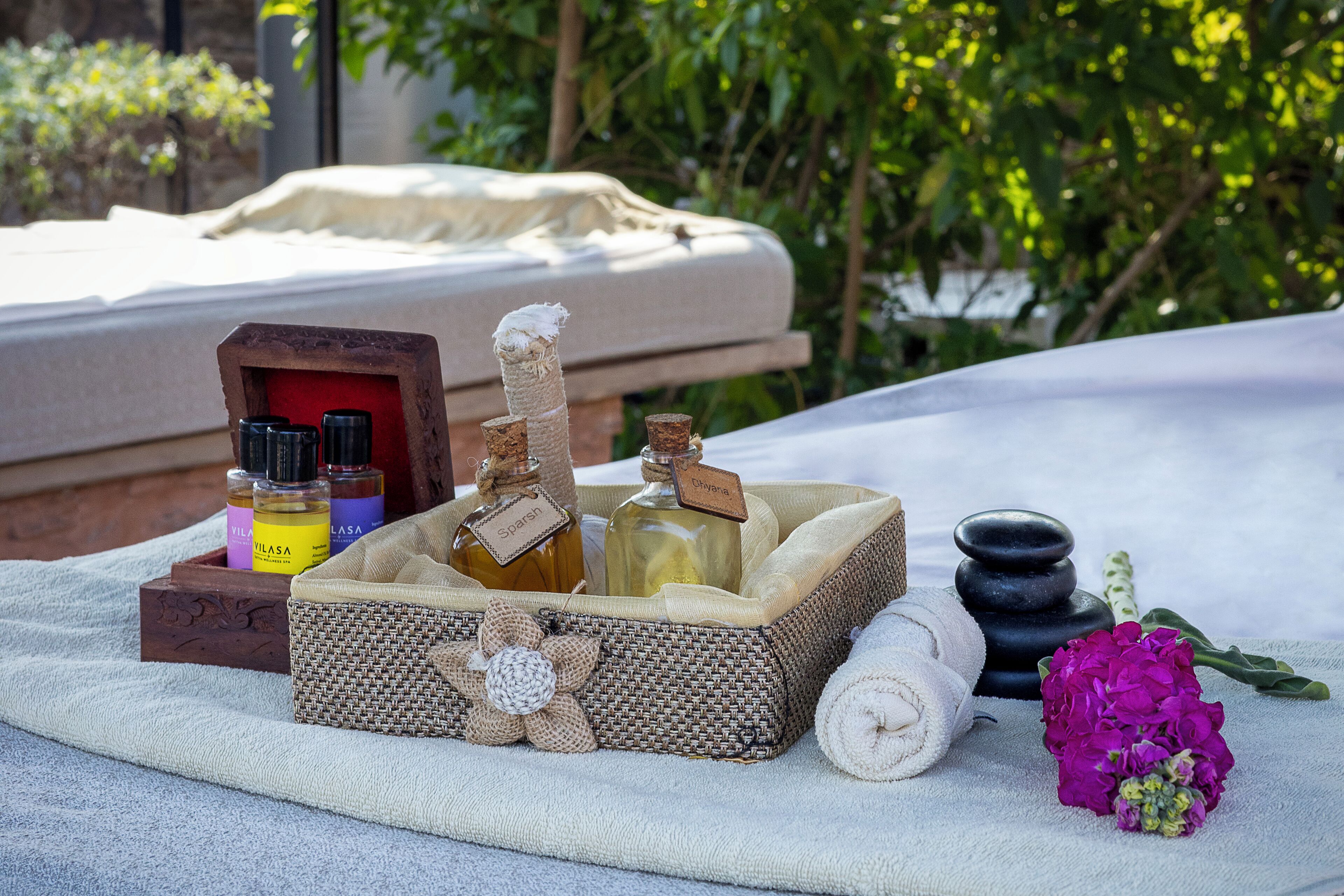 A spa setup with a massage table, bottles of essential oils, a rolled towel, and a flower.