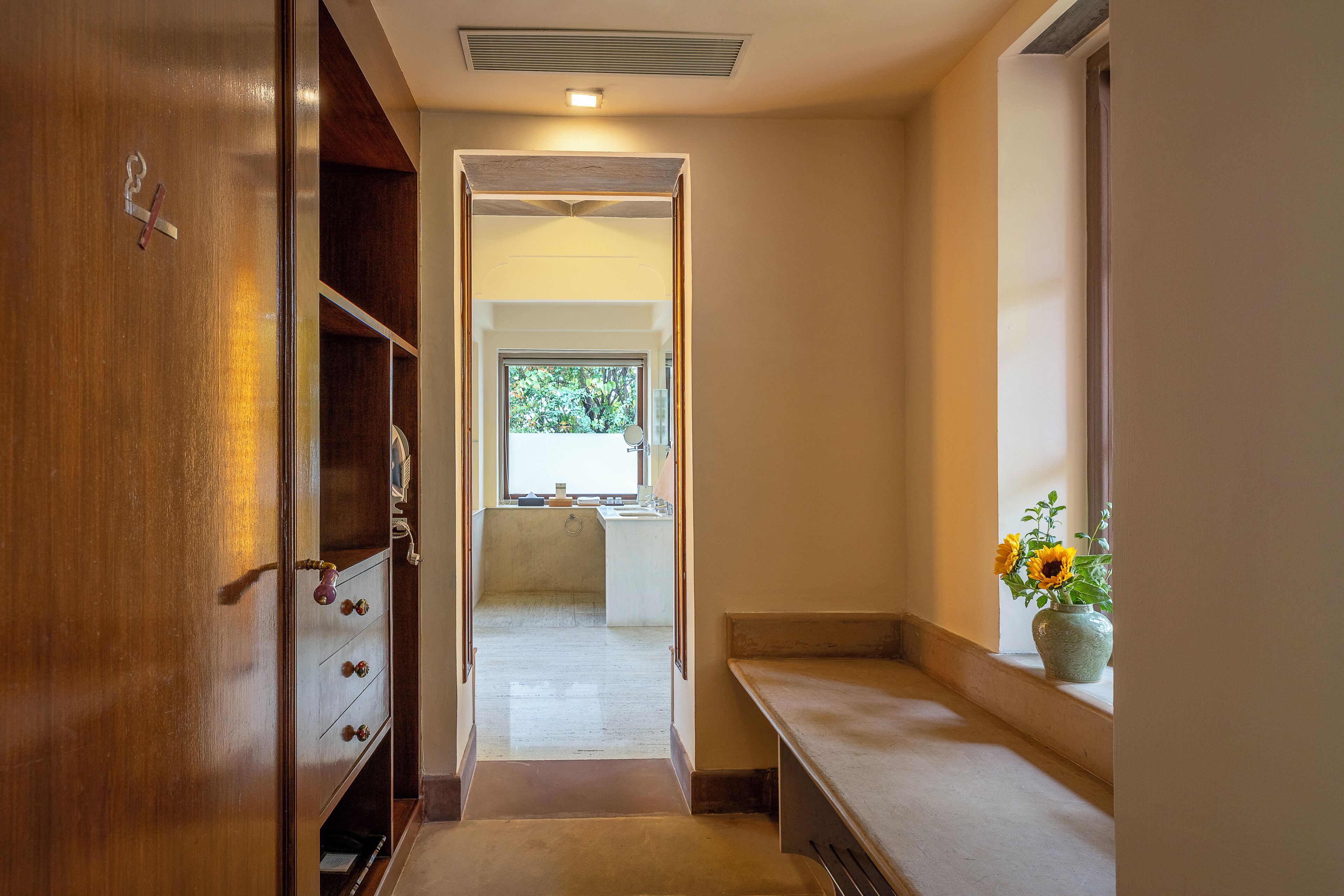 Um corredor com porta de madeira, um banco e um vaso com flores.