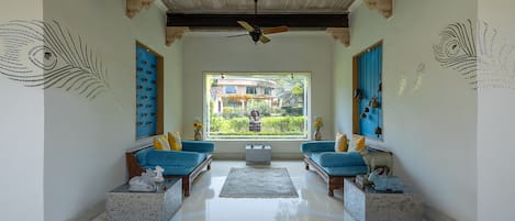 A spacious room with a large window, two blue sofas, a central rug, and decorative wall art.