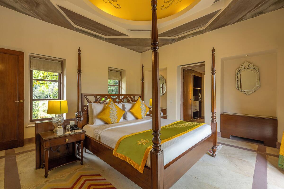 A four-poster bed with a wooden headboard, a bedside table with a lamp, and a mirror on the wall.