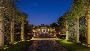 A formal garden pathway leading to a building with a central entrance, flanked by columns and illuminated lanterns. - The Tree of Life Resort & Spa, Jaipur (Amer)