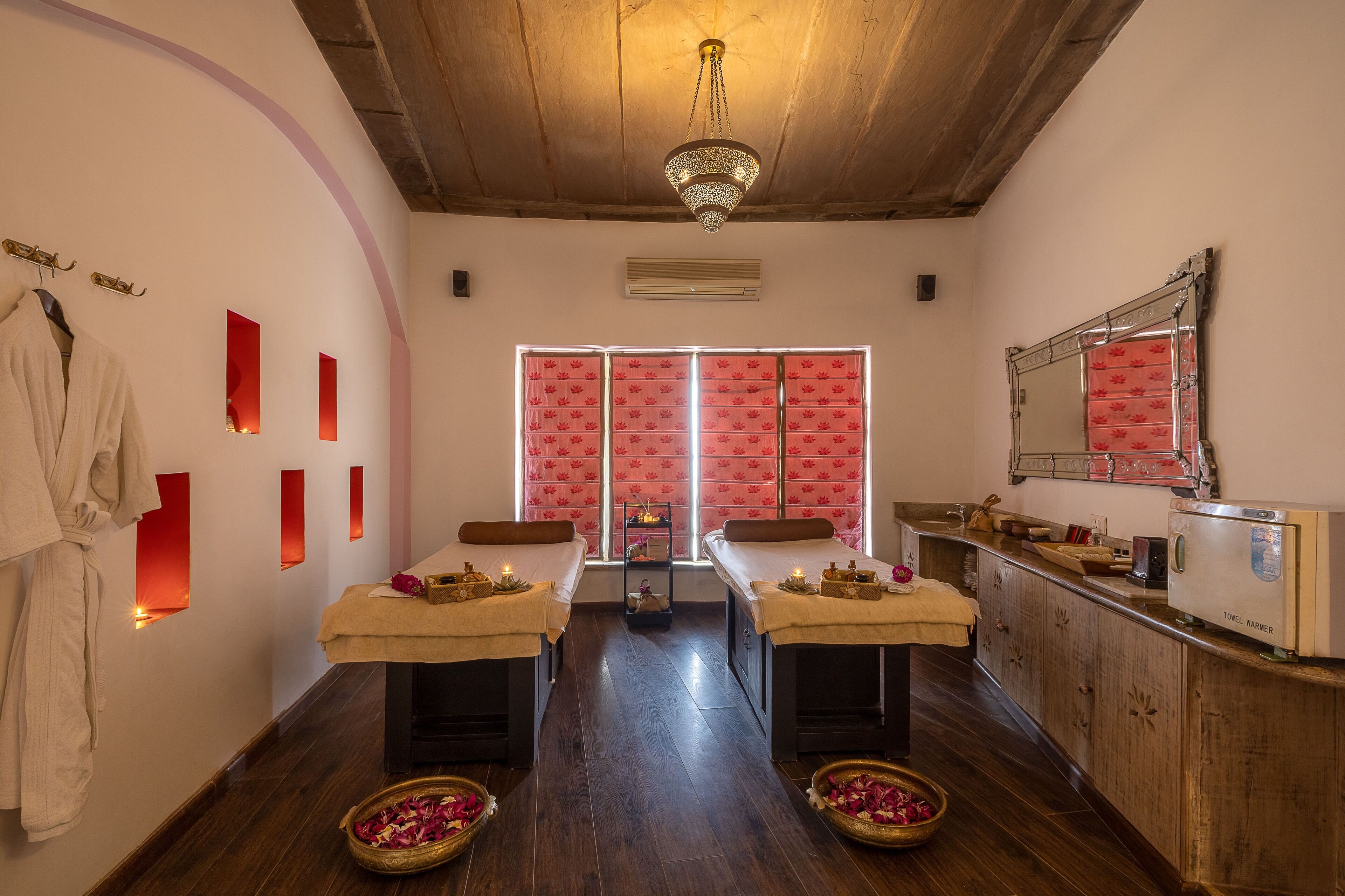 Um espaço de spa com duas macas de massagem, teto de madeira, espelho e porta-toalhas.