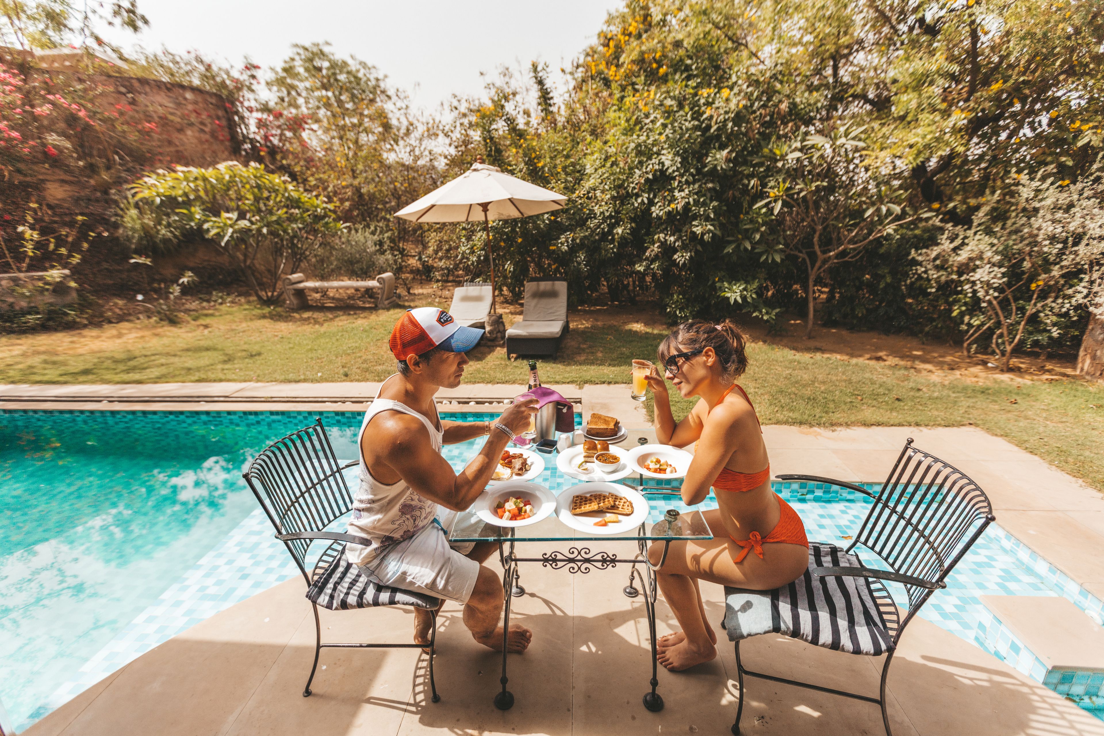 A poolside dining area with a table, chairs, and an umbrella.