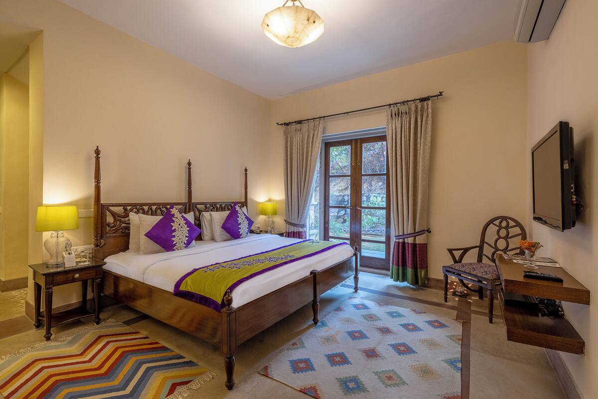 A hotel room with a bed, bedside tables, a desk, a chair, a television, and a window with curtains.