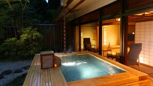 A hot spring bath area with wooden benches and a view of the interior through glass doors.