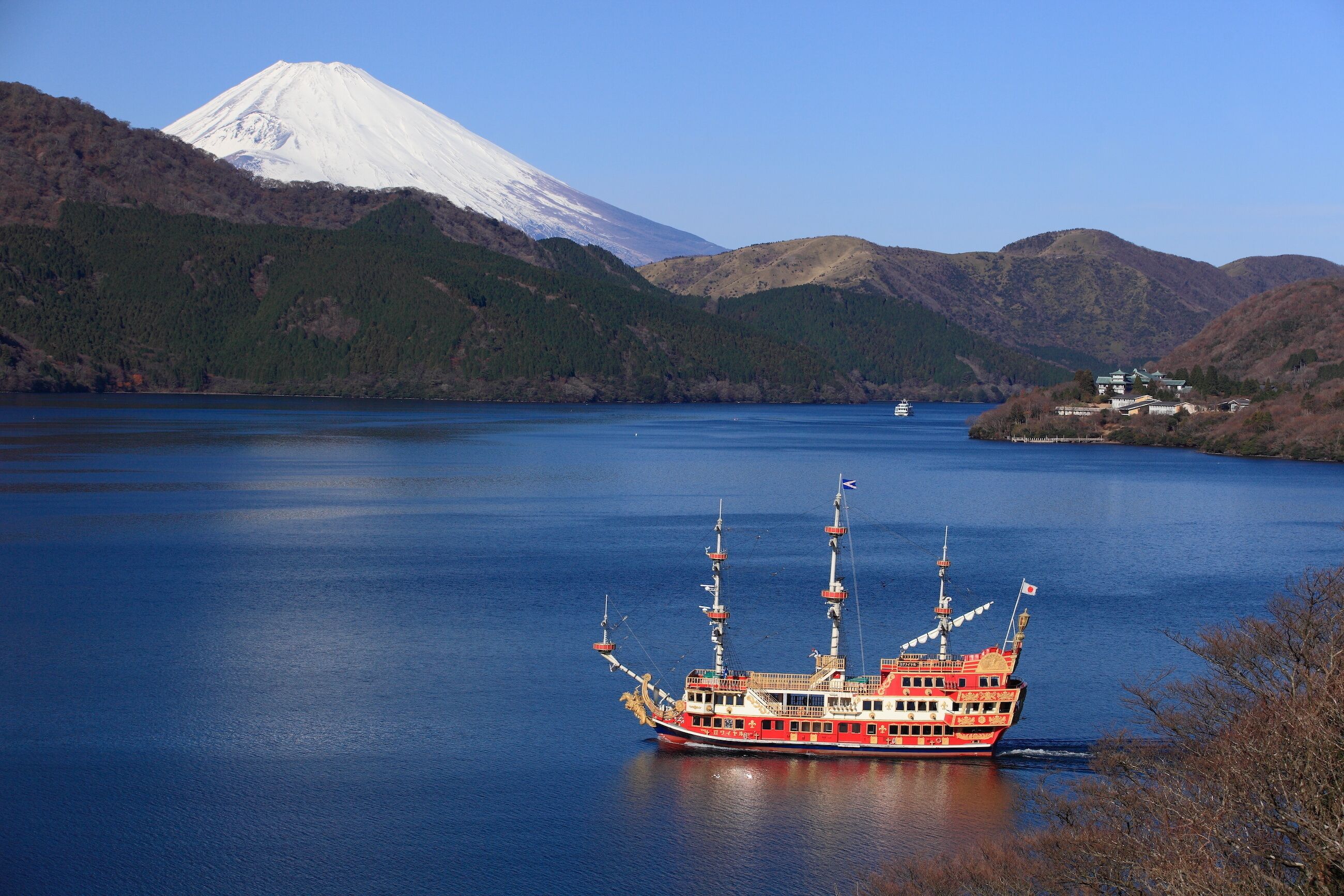 Un barco grande rojo y blanco en un lago tranquilo con una montaña al fondo.