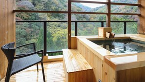 A wooden spa area with a hot tub, a wooden bench, and a chair, overlooking a forested hillside.