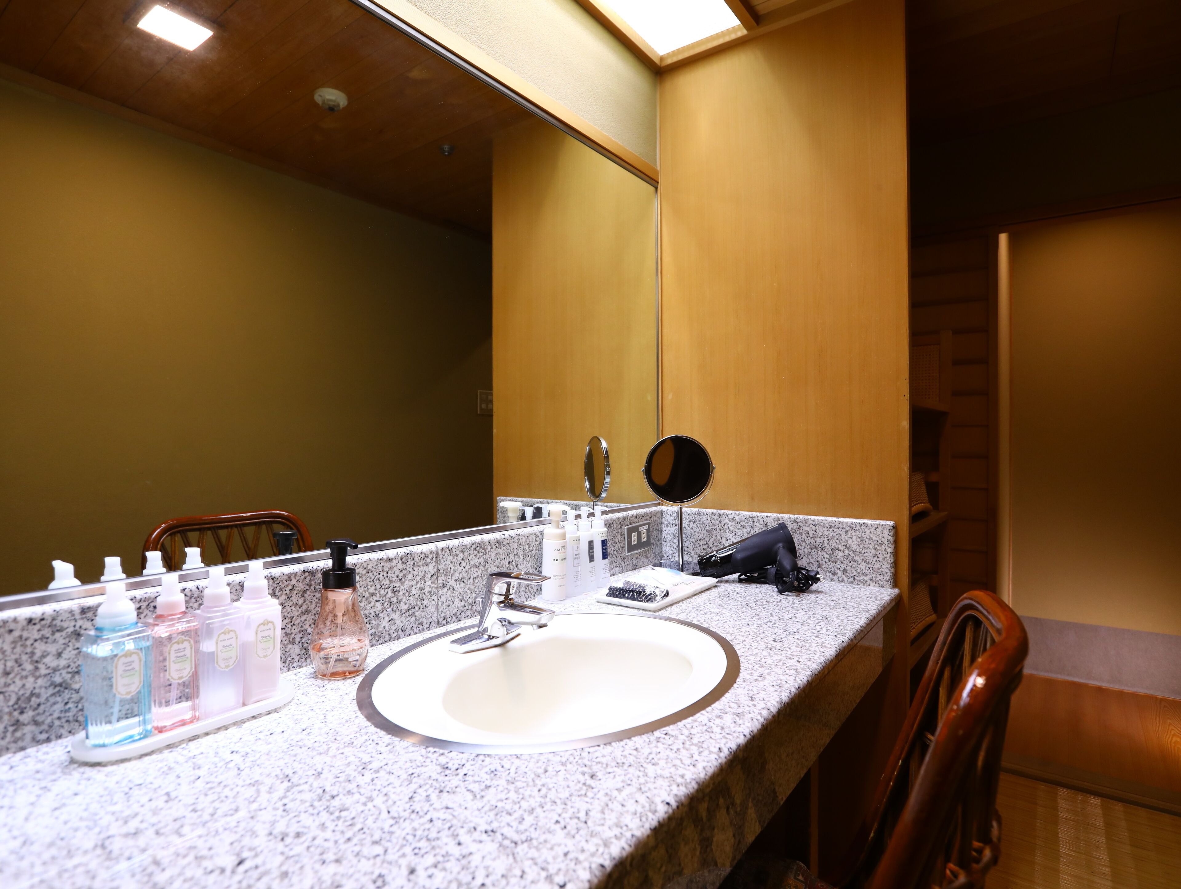 A hotel bathroom with a granite countertop, a sink, a mirror, and toiletries.