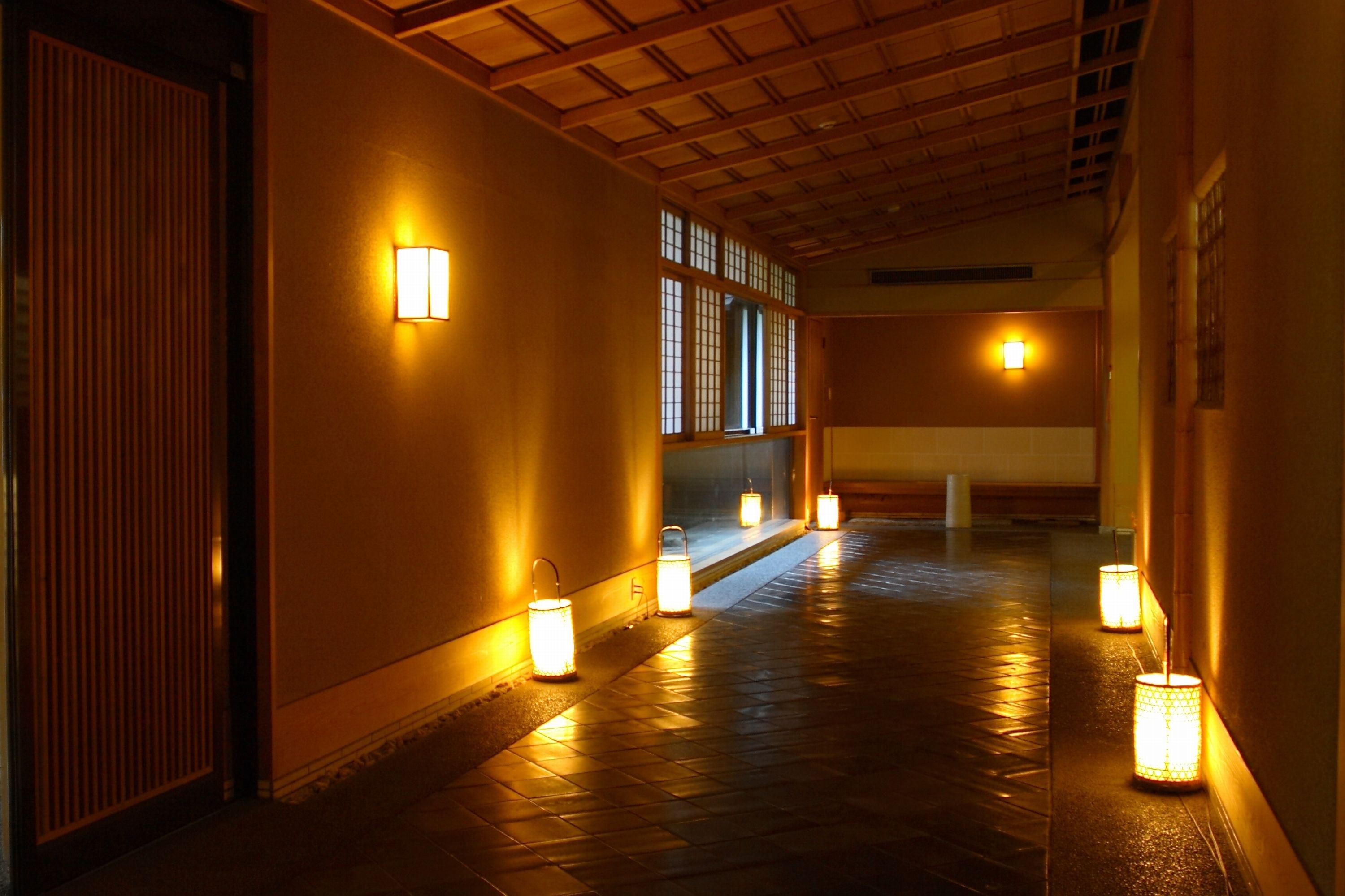 Un couloir orné de lanternes traditionnelles, de poutres en bois et de portes coulissantes.