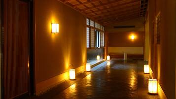 Un couloir orné de lanternes traditionnelles, de poutres en bois et de portes coulissantes.