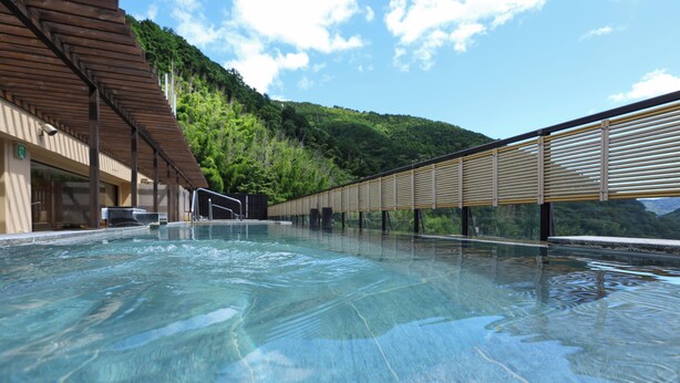 A clear indoor swimming pool with a wooden deck and a view of a forested hillside.