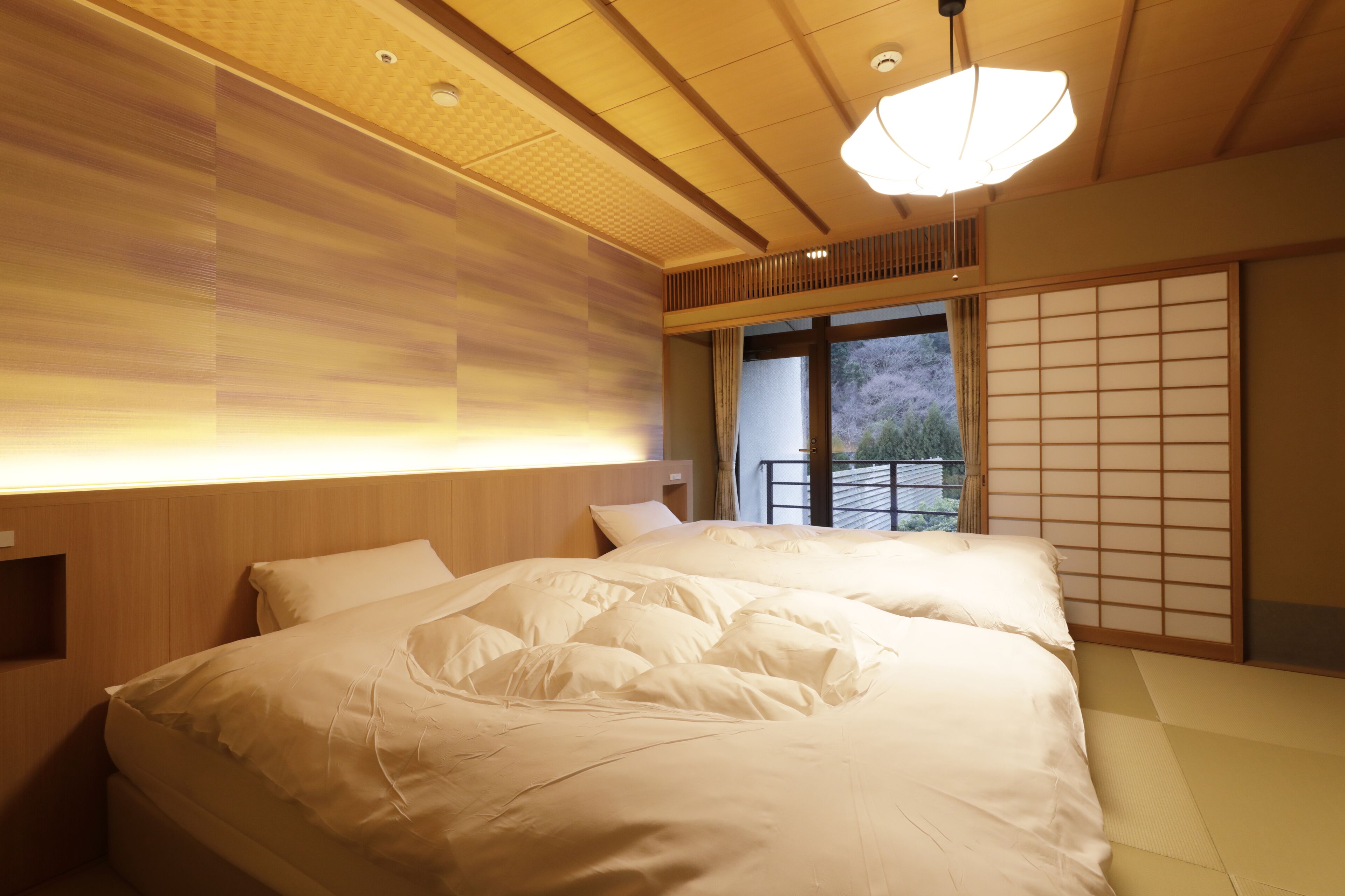 Een hotelkamer met een groot bed, een houten hoofdeinde en uitzicht buiten via een schuifdeur.