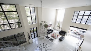 A spacious living area with large windows, a chandelier, and a modern floor design.