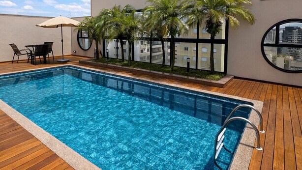 A swimming pool with wooden decking, palm trees, and a view of a cityscape.