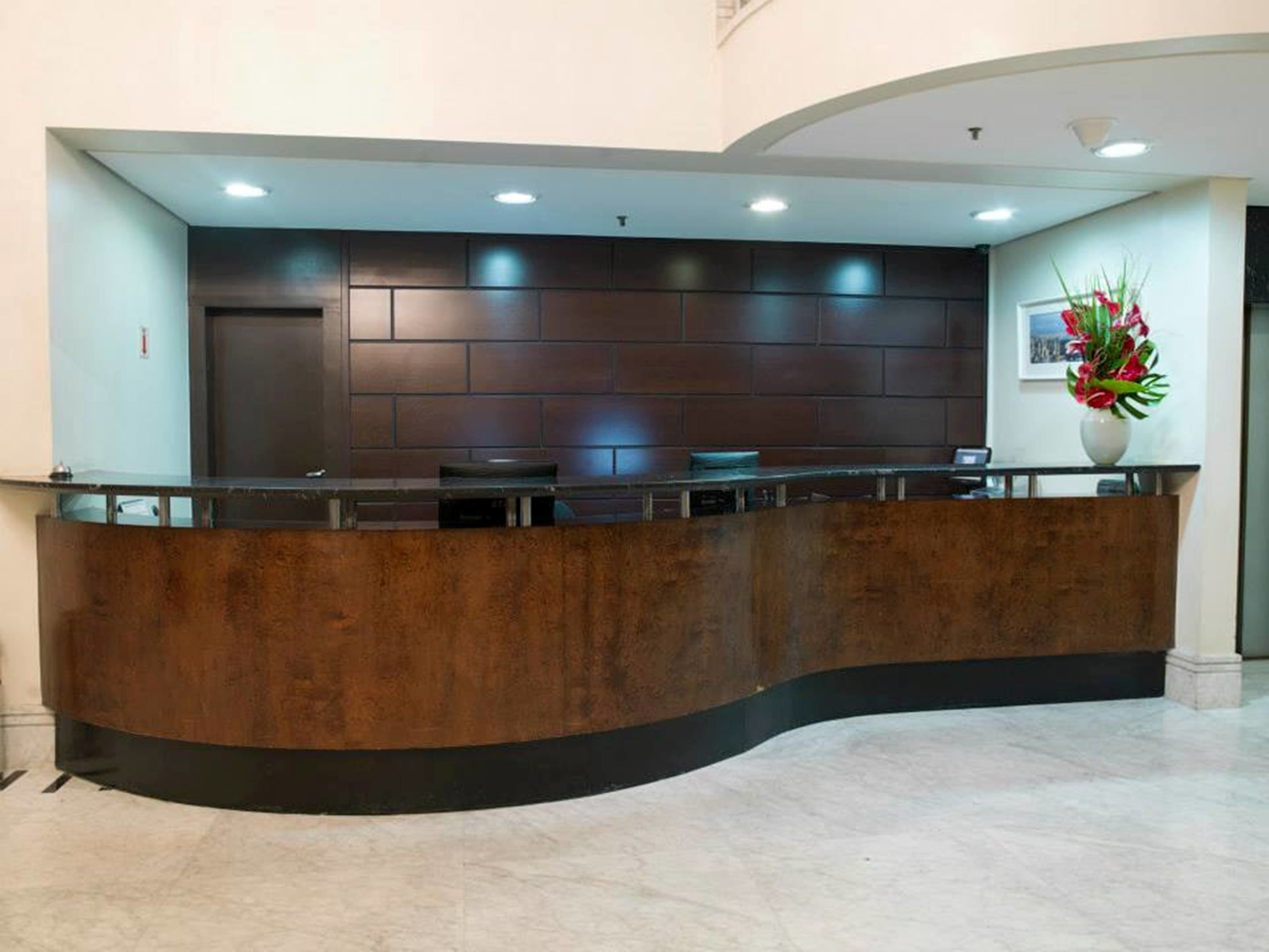 A reception desk with a curved design, a dark wooden finish, and a marble floor.