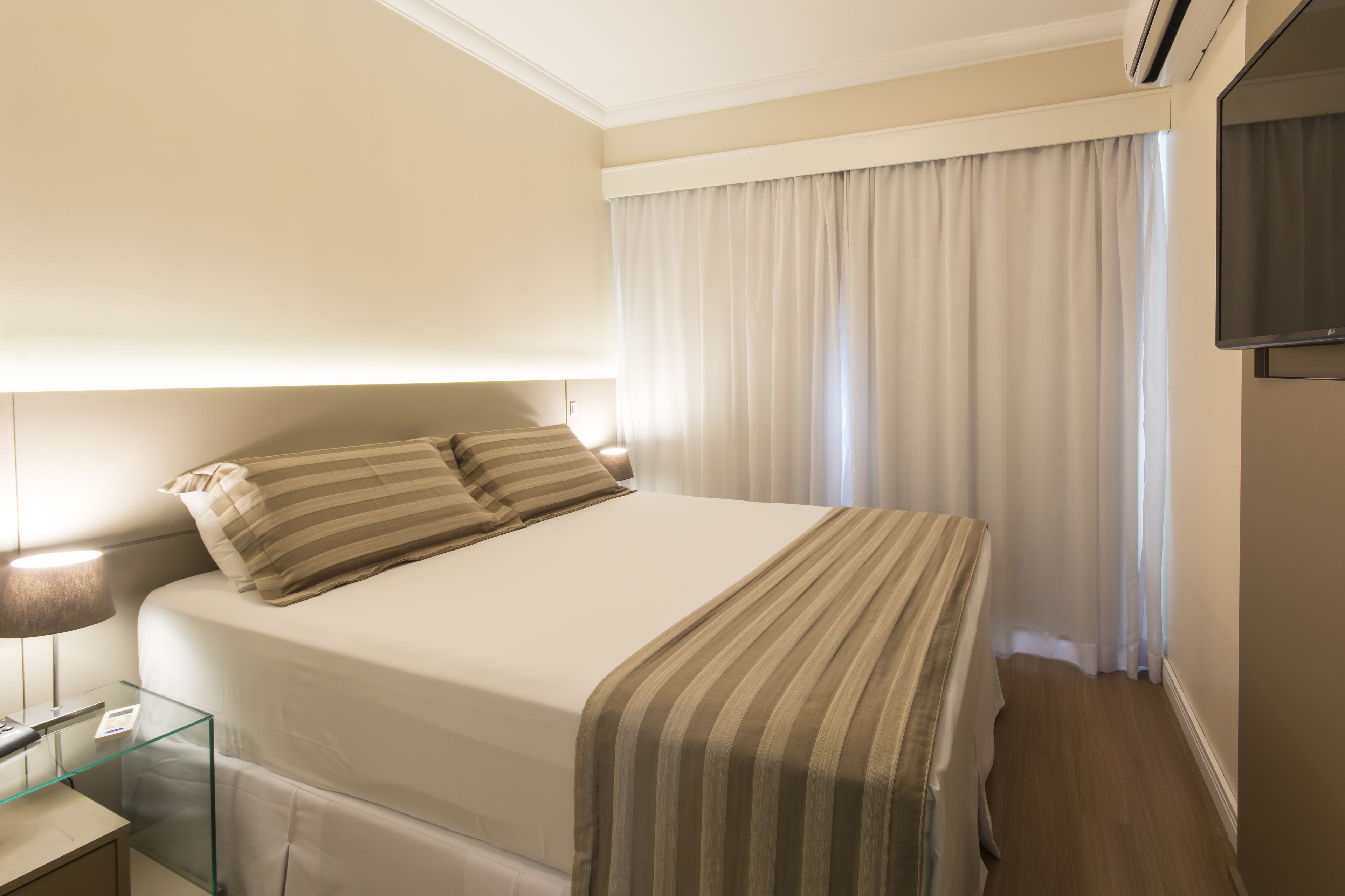 A hotel room with a bed, a bedside table with a lamp, a TV, and a window with curtains.