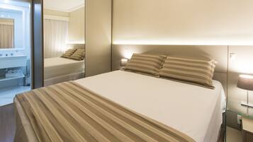 Habitación de hotel con una cama grande, una mesita de noche, un espejo y un baño con lavamanos y toallero.
