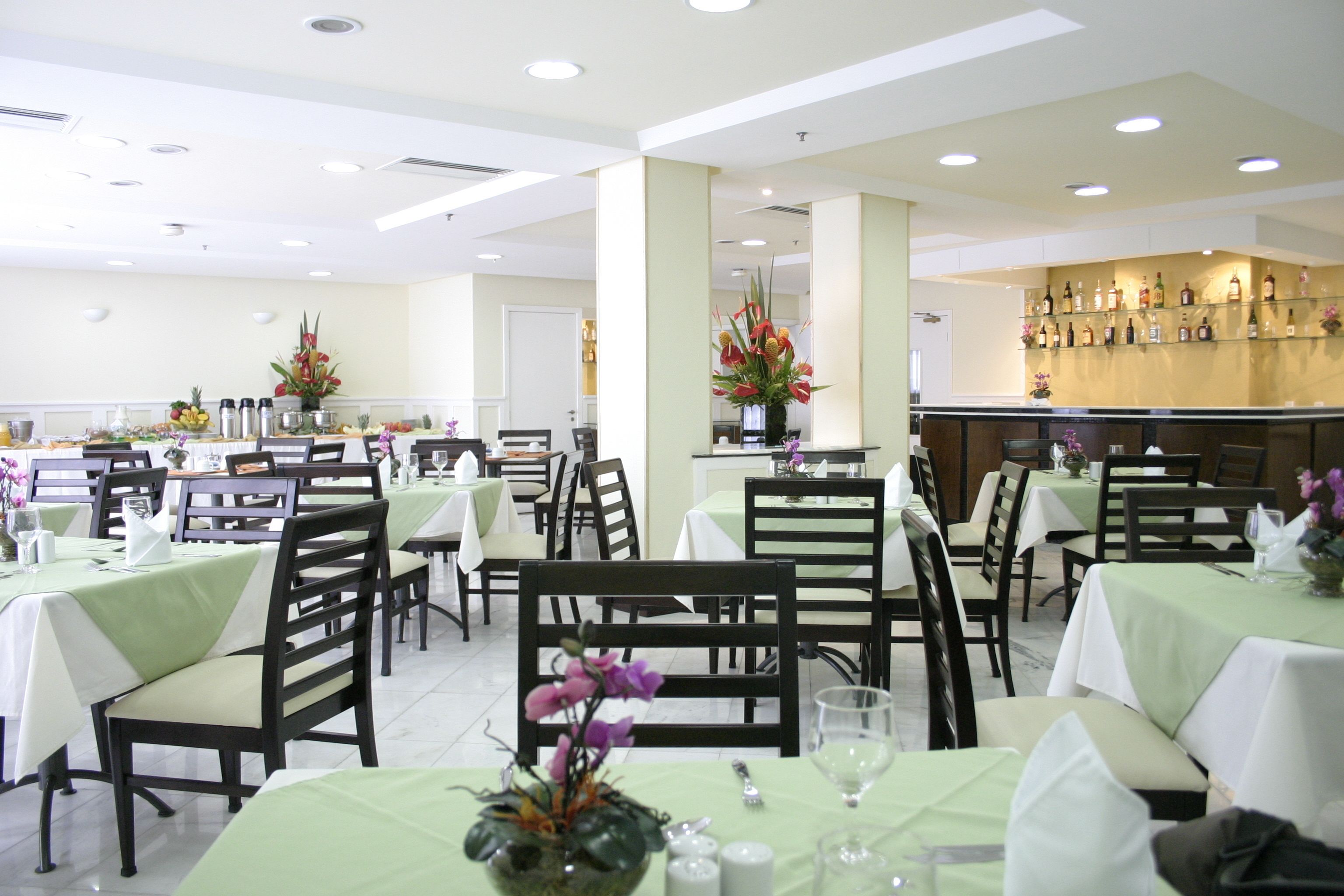 Un restaurante con varias mesas y sillas, una zona de bar y un arreglo floral decorativo.