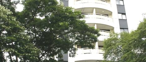 A multi-story building with balconies, a glass entrance, and surrounding trees.