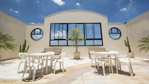 A courtyard with a large window, white chairs, and potted plants.