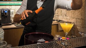 A bartender pouring a drink into a martini glass at a bar with shelves of liquor bottles in the background. - Dream Village (Hersonissos)