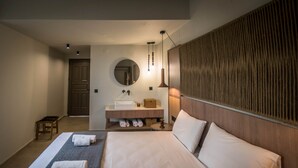 A hotel room with a large bed, a round mirror, a wooden headboard, a bedside table, and a small stool. - Dream Village (Hersonissos)