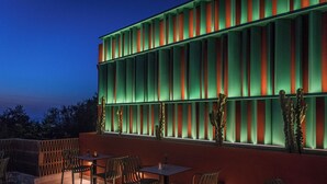 An outdoor seating area with tables and chairs, a cactus decoration, and a building with vertical lighting. - Dream Village (Hersonissos)