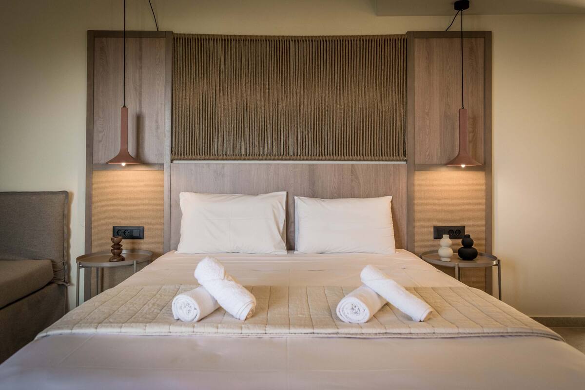 A neatly made bed with two pillows, a bedside table with a lamp, and a wall-mounted panel above the bed.