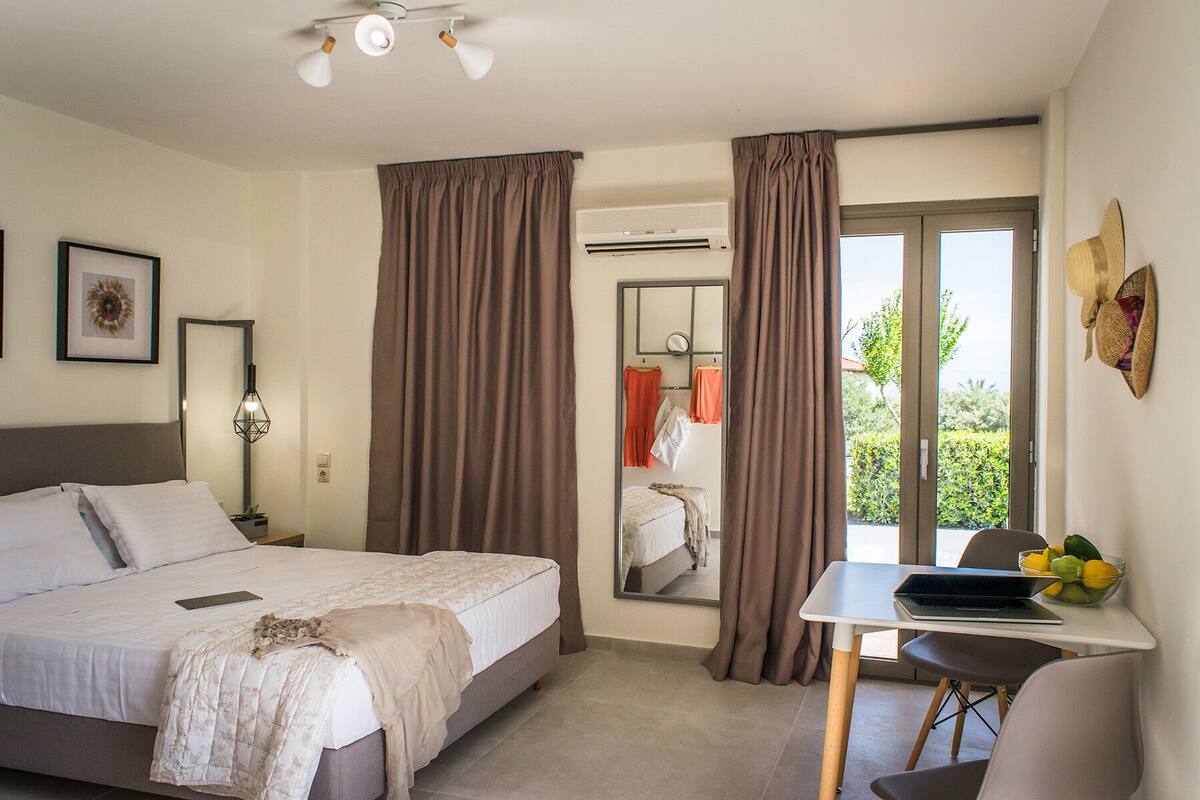 A hotel room with a bed, a desk with a laptop, a mirror, and a window with curtains.
