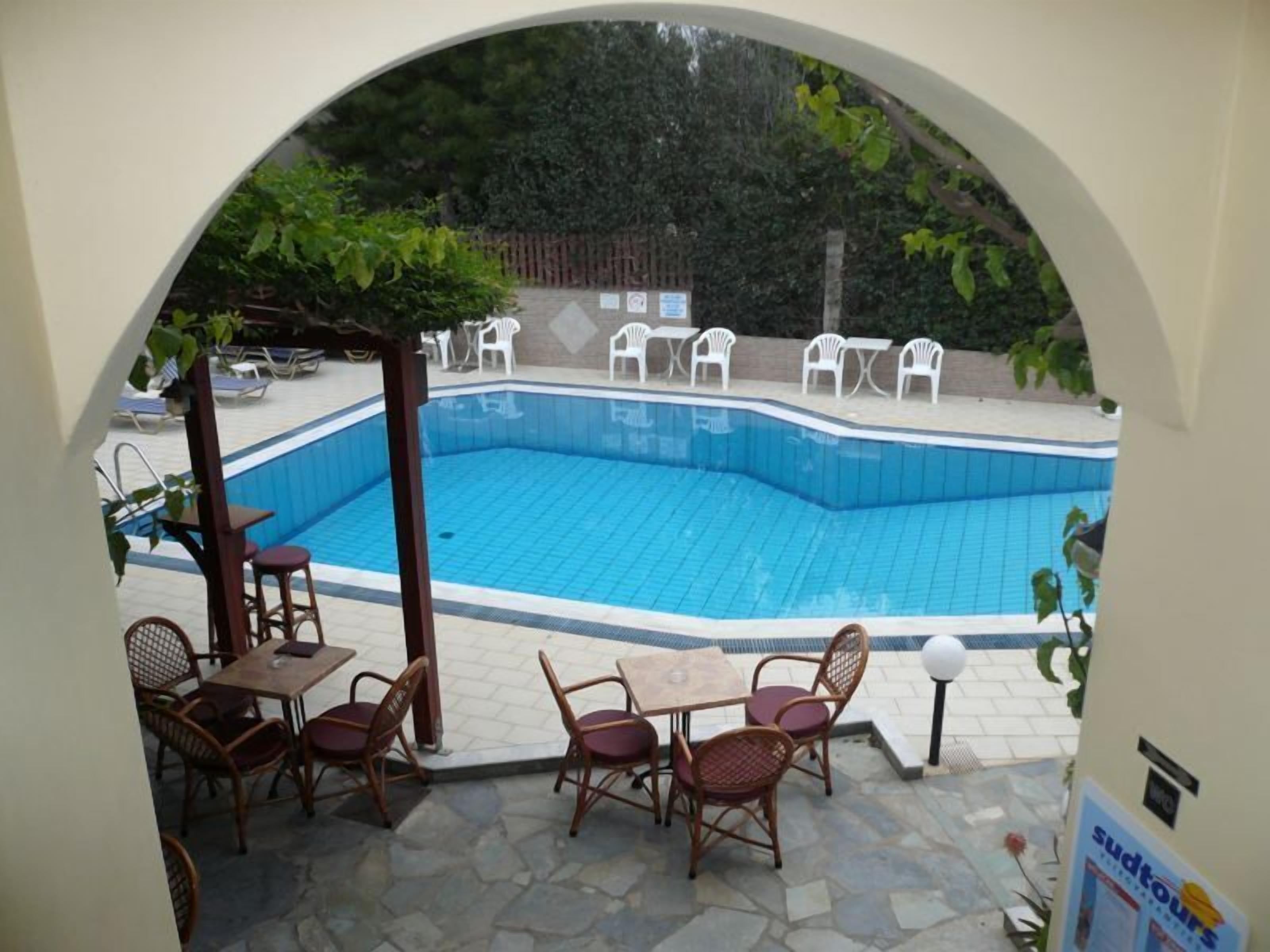 A swimming pool with a tiled deck, surrounded by outdoor furniture and a pergola.