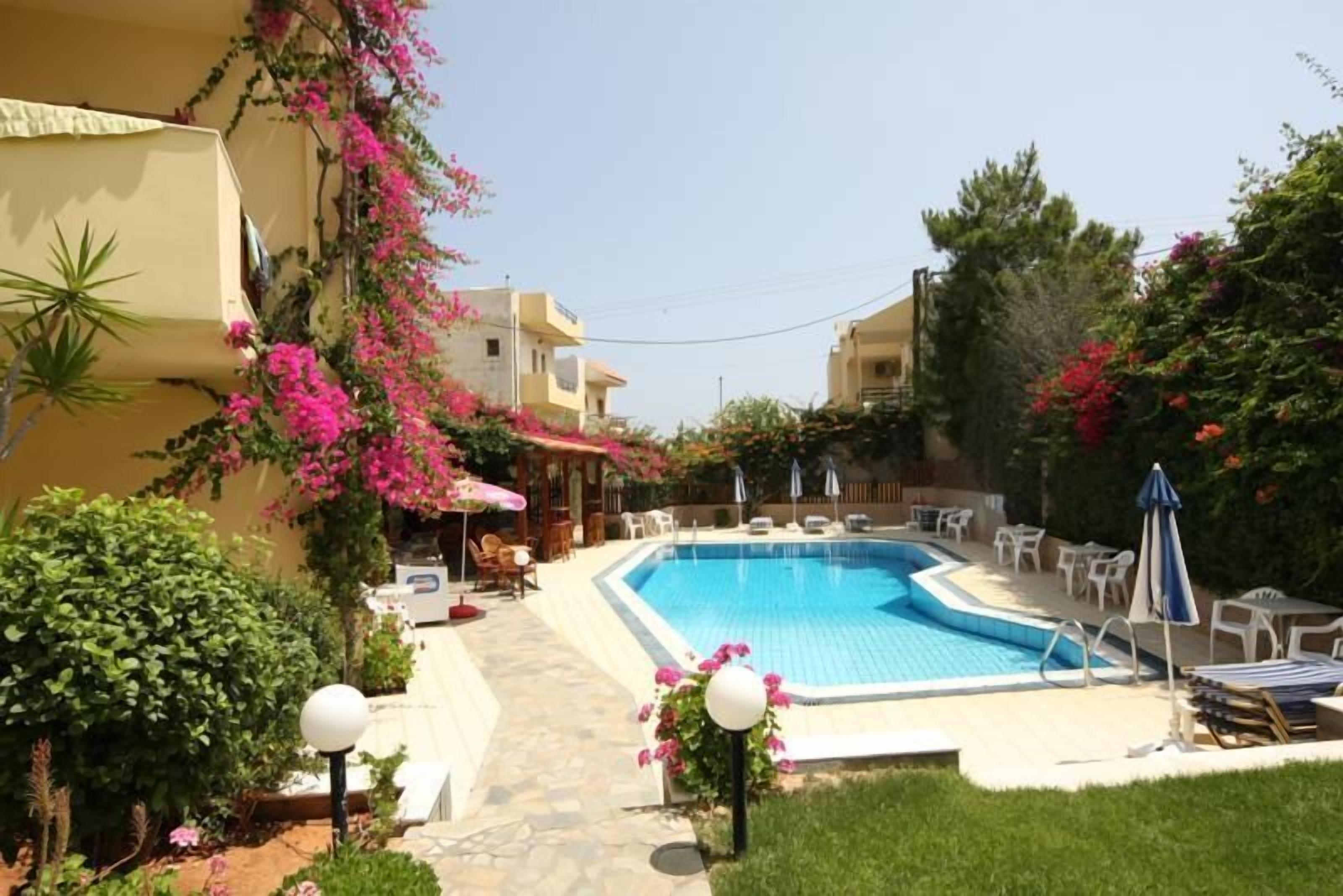 A swimming pool with lounge chairs and umbrellas, surrounded by greenery and pink flowers.