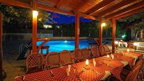 An outdoor dining area with tables and chairs, a pool, and a wooden pergola. - Maria Lambis Apartments (Hersonissos)