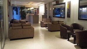 A modern lobby with sofas and armchairs arranged for seating, a reception desk, and large windows with artwork. - Maria Lambis Apartments (Hersonissos)